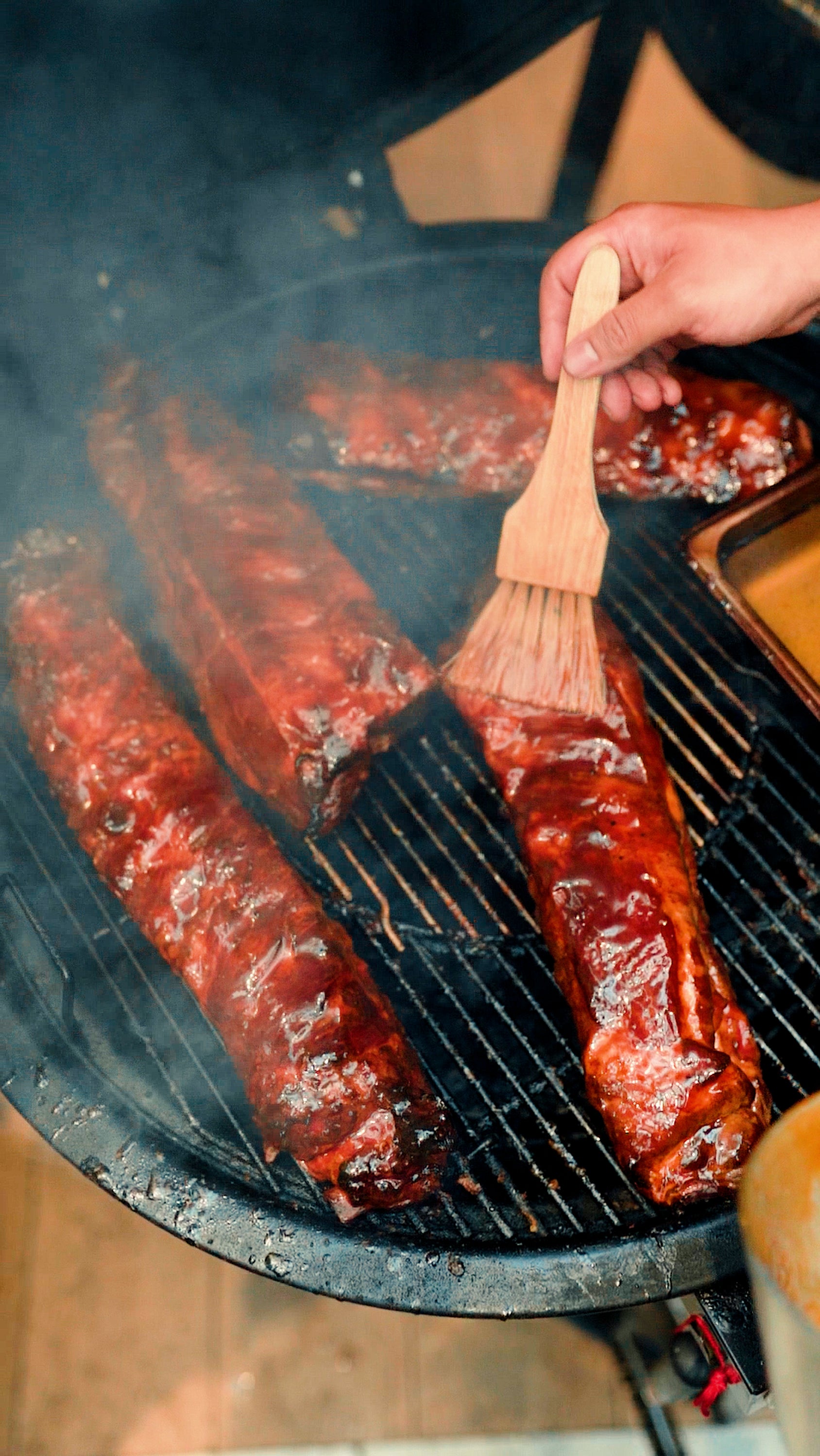 Mano unta costillas ahumadas en parrilla, ideal para asados y BBQ con astillas de madera