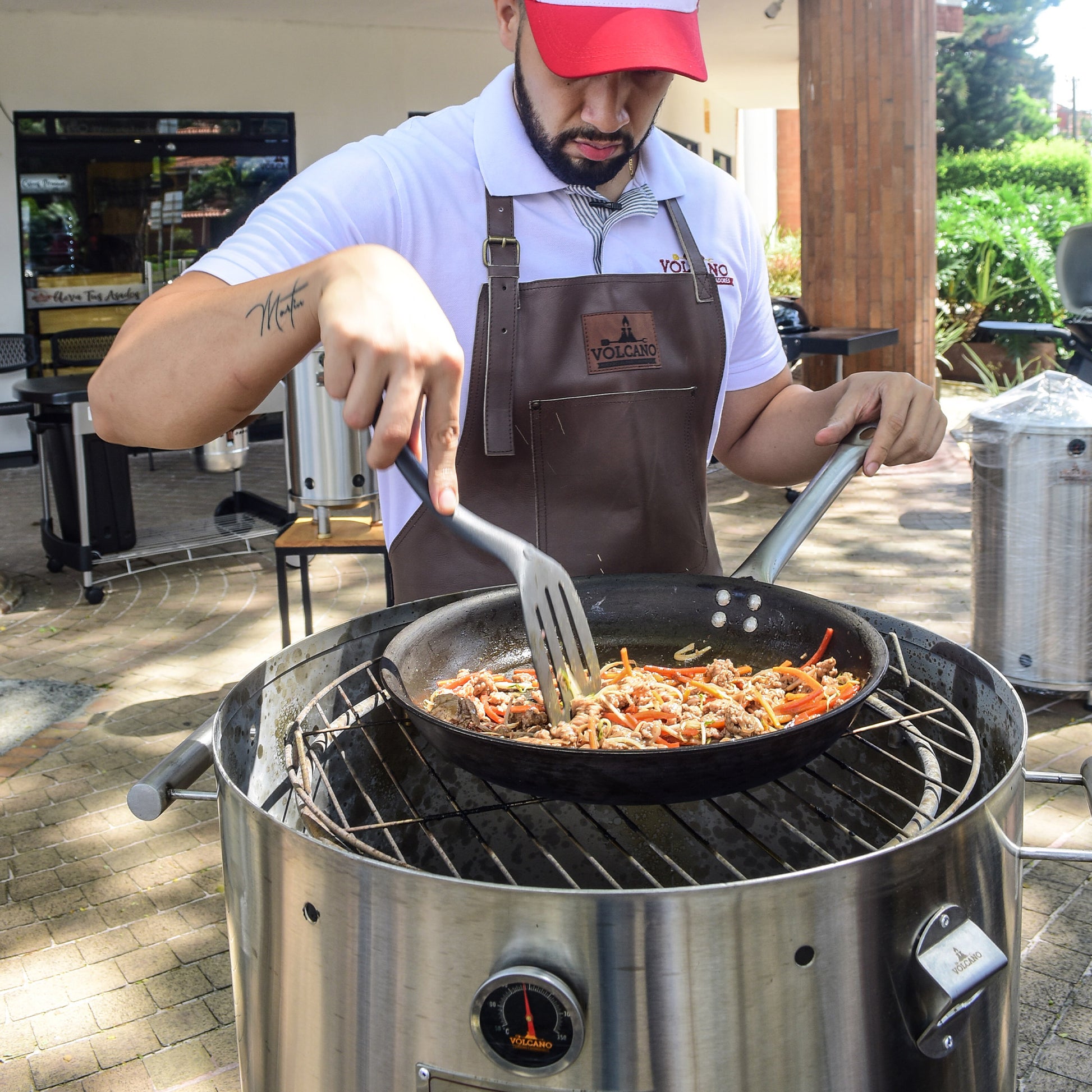 Hombre cocina carne y verduras en sartén sobre barril asador de acero inoxidable